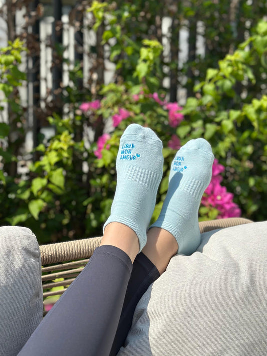 Light blue socks with text on a person sitting outdoors with greenery and flowers in the background.